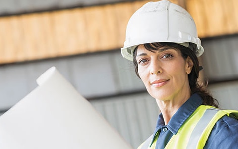 Woman wearing a construction hard hat and holding plans.